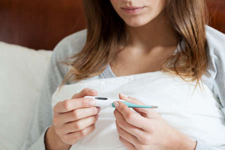 Sick woman in bed checking temperature