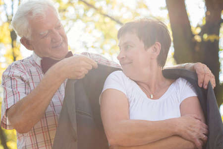 Elderly freezing woman with his caring husband in parkの写真素材