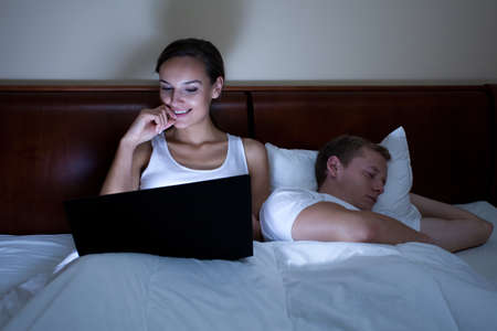 An awake woman on her laptop and her boyfriend asleep