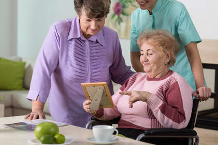 Two aged women and young therapist looking at picture