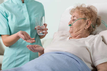 Young nurse giving the pills to sick aged womanの写真素材