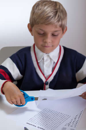 Blonde kid holding scissors and cutting paperの写真素材