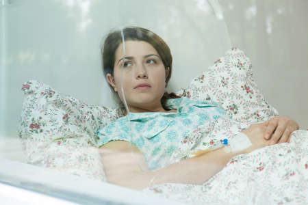 Ill young woman lying in hospital bedの写真素材