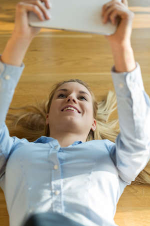 Young pretty woman lying on the floor holding the tabletの写真素材