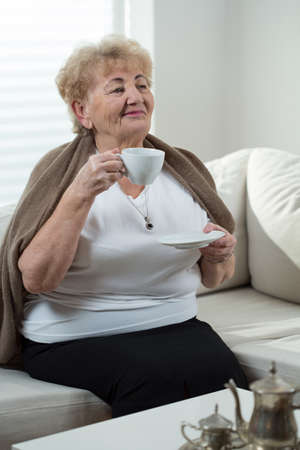 Senior woman sitting on the couch and drinking coffeeの写真素材