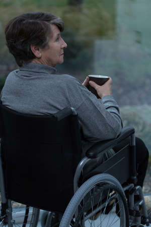 Senior pensive woman on wheelchair drinking hot teaの写真素材