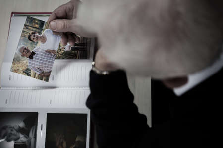 Lonely windowed man watching photo album and recollectingの写真素材