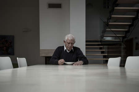 Elderly man eating dinner completly alone in huge house