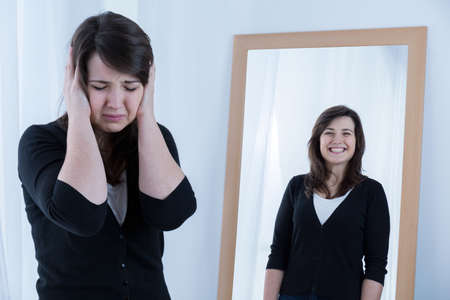 Young crying woman and her happy reflectionの写真素材