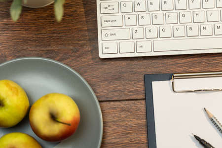 Keyboard, clipboard and apples on office deskの写真素材