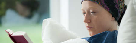 Woman with cancer reading a book in bedの写真素材