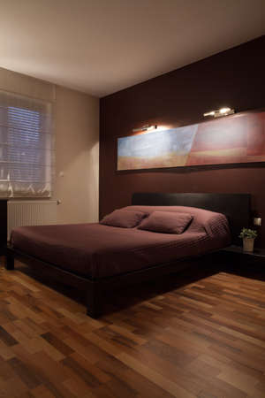 Big double bed in modest bedroom with wooden floorの写真素材