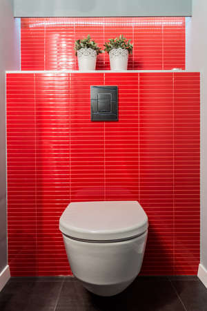 White toilet bowl on wall of red tiles