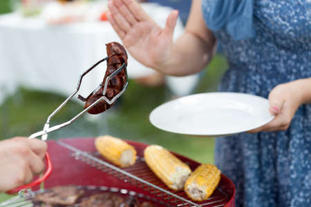 Woman refusing frazzled sausage on barbecue partyの写真素材