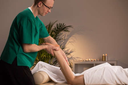 Masseur massaging lower limb of young womanの写真素材