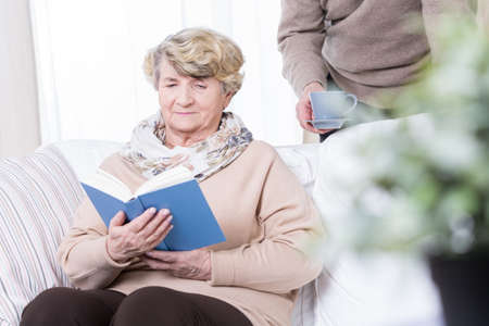 Senior woman sitting on the sofa and reading bookの写真素材
