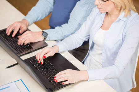Elderly people sitting at the desk and working on laptops