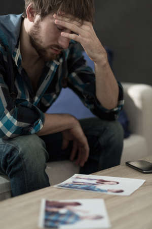 Young heartbroken man looking pictures with ex-girlfriendの写真素材