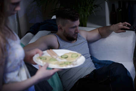 Sad tired wife serving sandwiches to her lazy husbandの写真素材