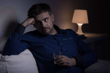 Worried troubled man holding glass of waterの写真素材