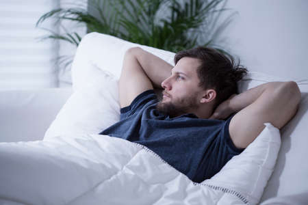 Young handsome man lying in bed at dayの写真素材