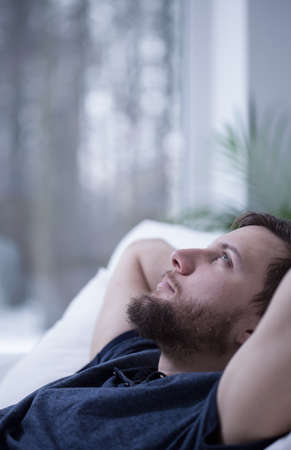 Close-up of young handsome thoughtful man in bedの写真素材