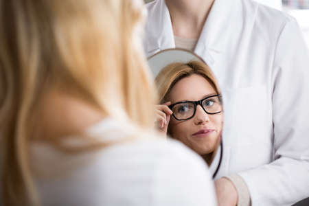 Young pretty woman in glasses admiring her reflection in mirrorの写真素材