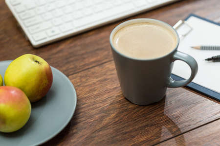 Plate of healthy snacks and cup of hot coffee on office deskの写真素材