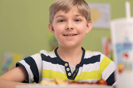 Happy smiling boy eating breakfast in classroomの写真素材
