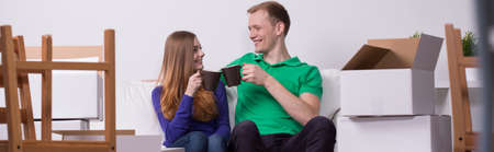 Smiling couple drinking tea in new house - panorama