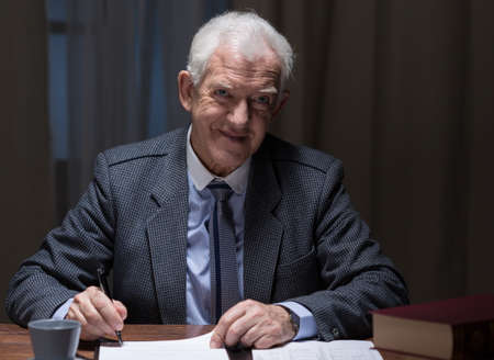 Smiling aged man working in the evening in his officeの写真素材