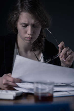 Overworked woman doing paperwork and drinking alcoholの写真素材