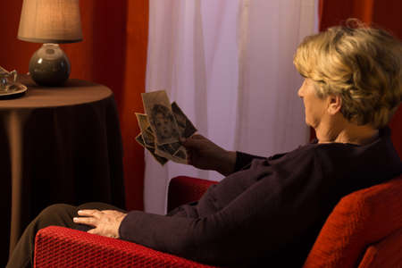 Senior thoughtful lady looking at old photos from childhoodの写真素材