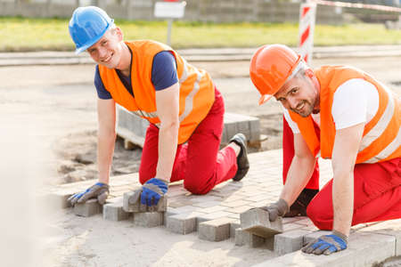 Two smiling construction workers laying new cobblestonesの写真素材