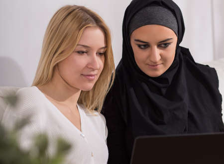Blonde woman and muslim girl using laptopの写真素材