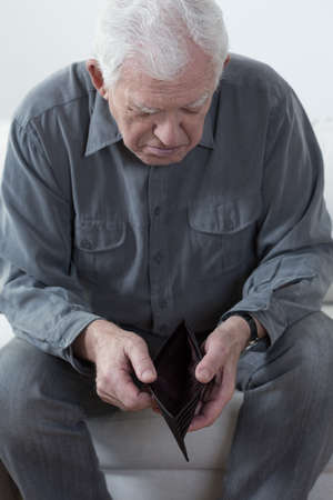 Old man sitting on a couch and looking at an empty walletの写真素材