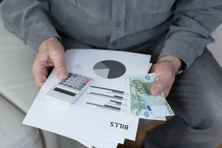 Old man with financial difficulties holding billsの写真素材