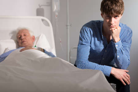 Young man sitting by his sick grandfatherの写真素材