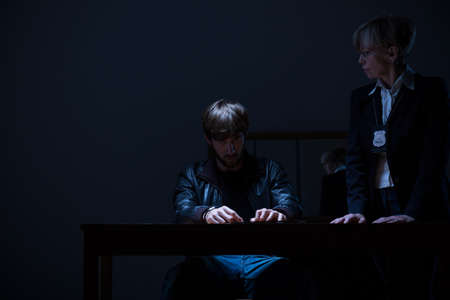 Guilty man and elderly policewoman in dark roomの写真素材