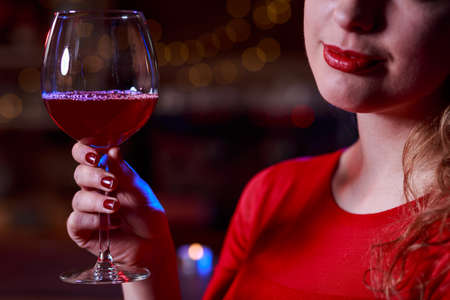 Young girl with curly hair is drinking red wineの写真素材