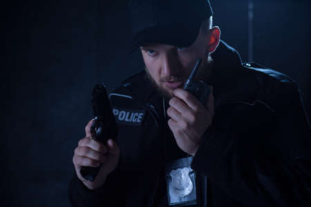 Image of a serious policeman holding radio and gunの写真素材
