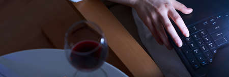 Close-up of glass of wine and woman writing on laptopの写真素材