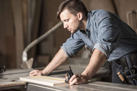 Young carpenter using measuring tape at work