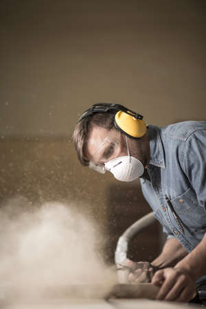 Carpenter wearing protective headphones while using electric sawの写真素材