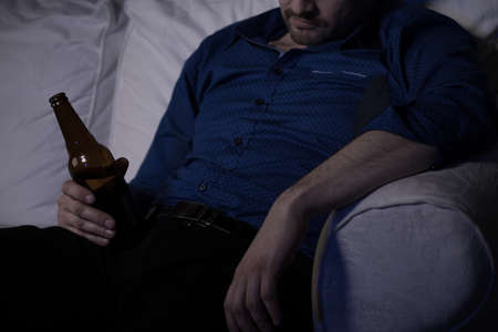 Tired man sleeping on couch with bottle of beer