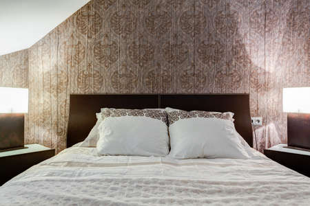 Comfortable bed and brown wallpaper in elegant bedroomの写真素材