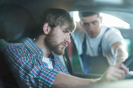 Man sitting in a car and talking with motor mechanicの写真素材