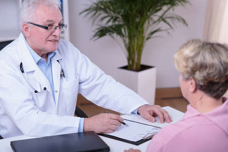 Aged experienced physician filling older patient's medical historyの写真素材