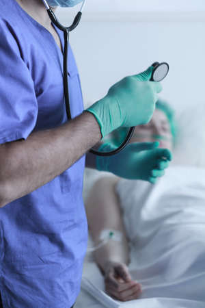 Doctor with stethoscope and lying patient in backgroundの写真素材