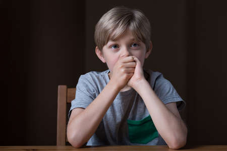 Photo of sad young boy covering mouth with handsの写真素材